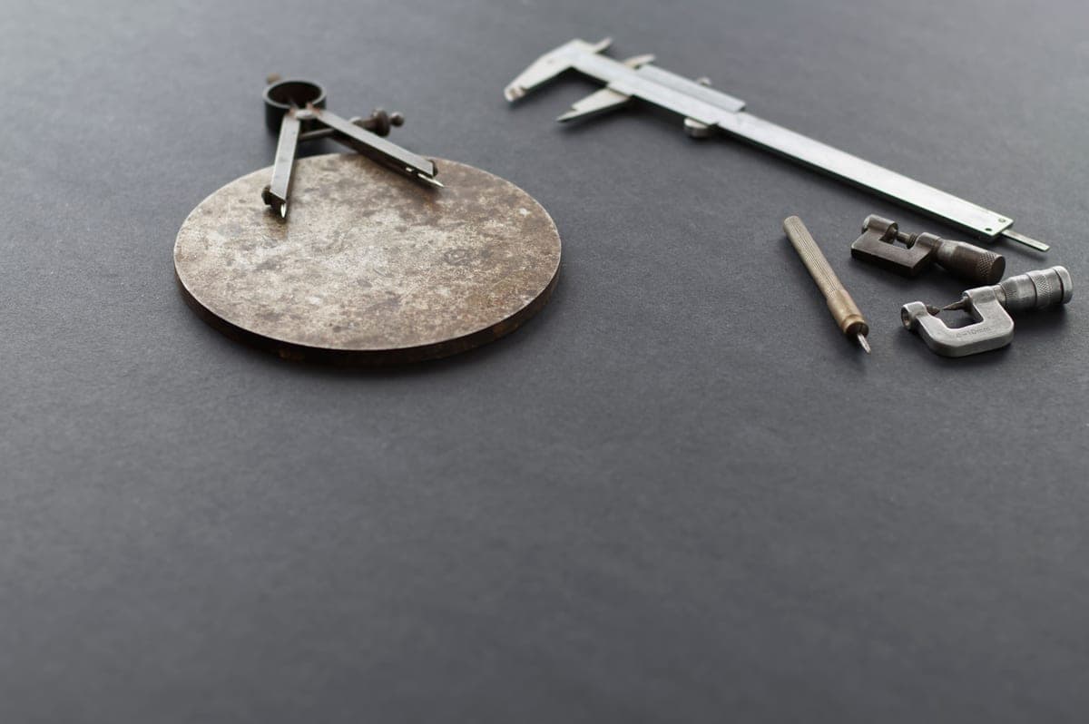 Calipers, a micrometer and a compass arranged on a dark gray work surface
